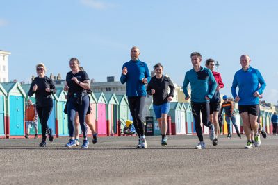 Men and women running besides a row of beach huts