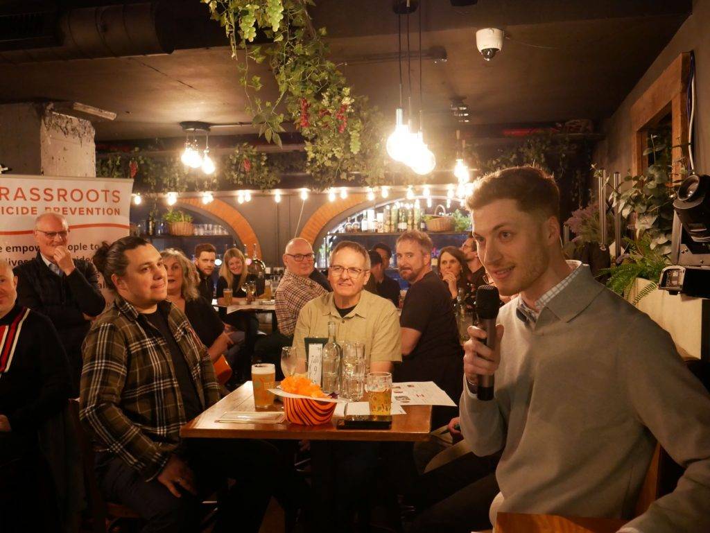 A group of people participate in a quiz in a bar. A man holds a microphone.