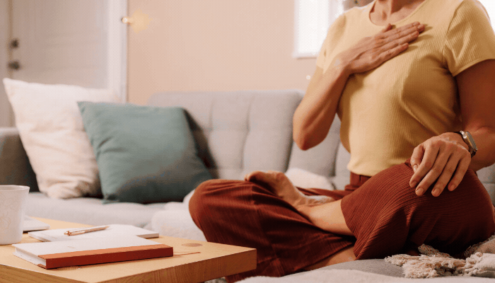 Woman with hand on chest sat on sofa. Breath in in text comes on and breath in text comes on