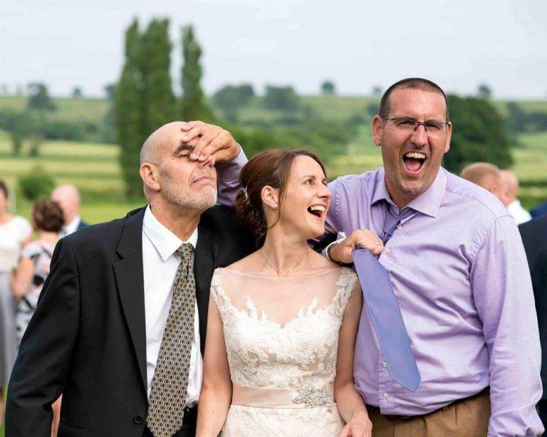 Three people at a wedding laughing.
