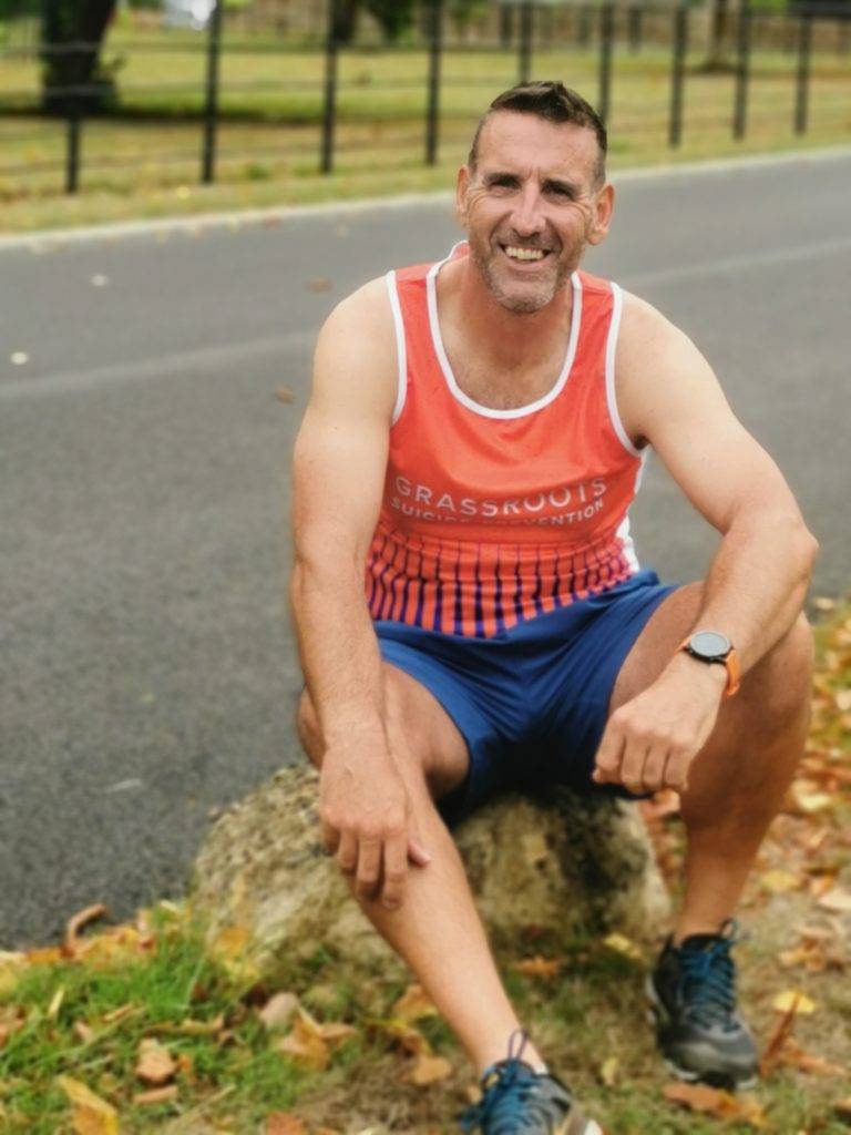 Man in orange vest and running outfit sitting on a rock.