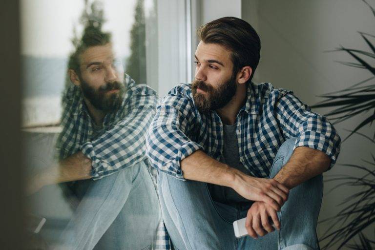 Thoughtful man relaxing on window sill at home. stock photo